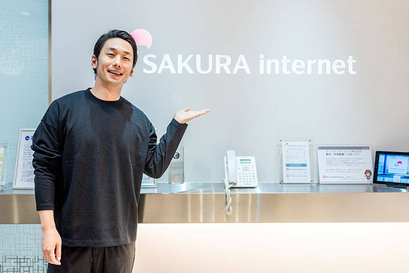 さくらインターネットのロゴ前で写真を撮る大川さん
